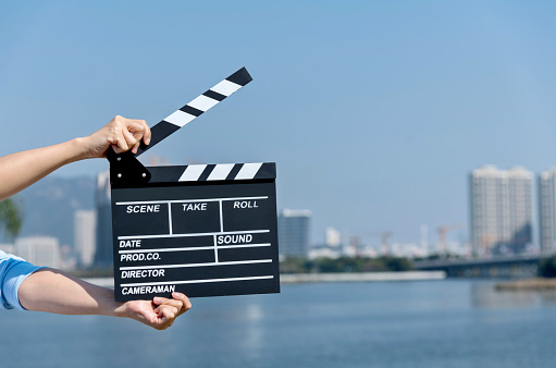 Hand is holding clapper board or clapperboard or movie slate, used in film production and cinema ,movies industry isolated over blue background.