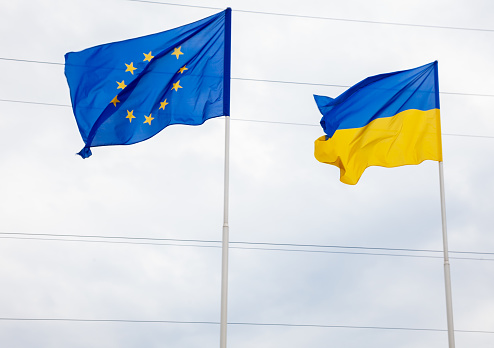 The flag of the European Union and Ukraine fluttering on the flagpole. Flags of Europe. Outdoor street background.