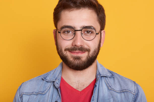 istock Indoor horizontal image of delighted good looking young man looking directly at camera, smiling sincerely, wearing spectacles, denim jacket and red t shirt, being in good mood. Emotions concept. 1237452672