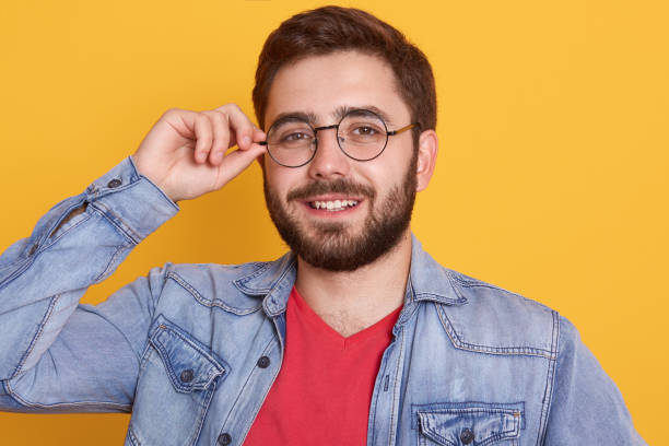 istock Studio portrait of cheerful magnetic bearded happy young man looking directly at camera, smiling sincerely, having pleasant facial expression, touching his eyewear. People and emotions concept. 1237452673