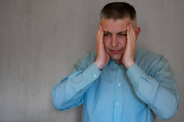 istock Middle aged man portrait touching his head temples with hands. 40 years man not looking at camera. Blue business shirt is dressed. Sad face and negative emotions 1237453243