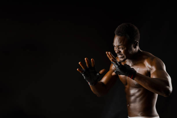 istock Athletic african fighter on black background. Dark skinned undressed man shows a fight. Advert for sport club and gym. Professional boxing and karate 1237459508