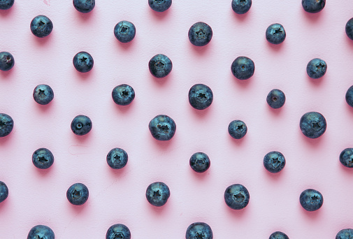 Fresh blueberries are laid out in a pattern on a lilac background with soft light and shadows, a bright poster