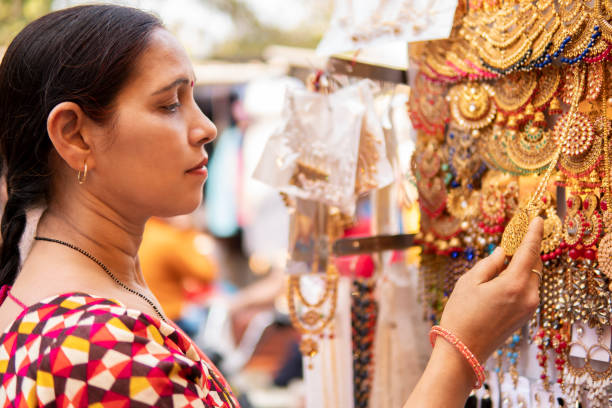 Indian mature woman shopping for earrings at outdoor street market. stock photo Indian mature woman looking and buying earrings, jewelry from outdoor street market of Delhi, India at day time. She is in her traditional Indian dress sari. india indian culture market clothing stock pictures, royalty-free photos & images