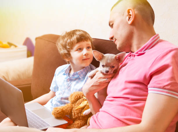 istock Happy young father sit on couch using laptop relax with preschooler son holding puppy chihuahua have fun together, smiling dad and little boy child enjoy weekend at home rest on sofa busy with gadgets 1237498897