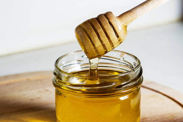 Honey with a wooden honey ladle drips on a wooden table stock photo