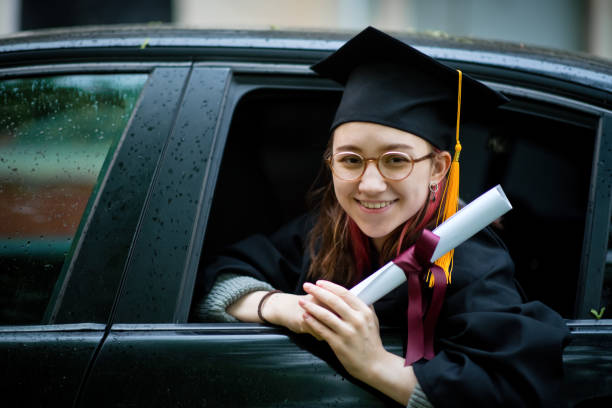 teenage girl wearing graduation gown and cap with diploma in car - university graduation car student imagens e fotografias de stock