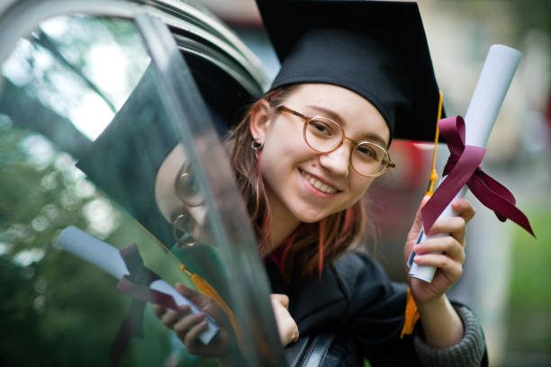 teenage girl wearing graduation gown and cap with diploma in car - university graduation car student imagens e fotografias de stock