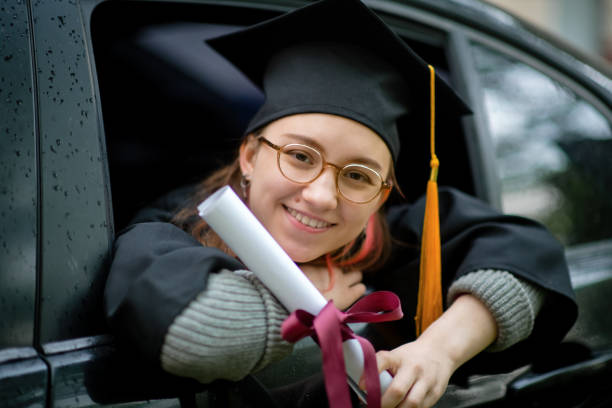 teenage girl wearing graduation gown and cap with diploma in car - university graduation car student imagens e fotografias de stock