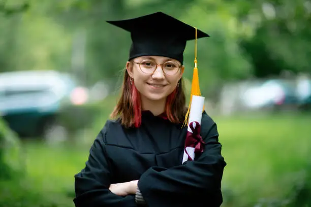 Photo of Teenage girl wearing graduation gown and cap with diploma