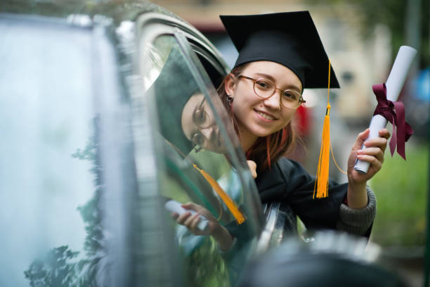 teenage girl wearing graduation gown and cap with diploma in car - university graduation car student imagens e fotografias de stock