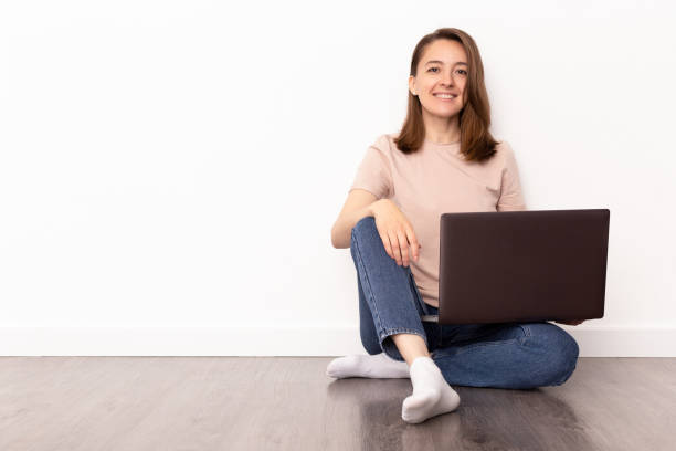 istock Smiling young woman sitting on the floor with laptop computer over white background 1237631585