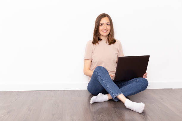 istock Young female with beautiful smile studying on laptop while sitting on the floor near white wall 1237632092