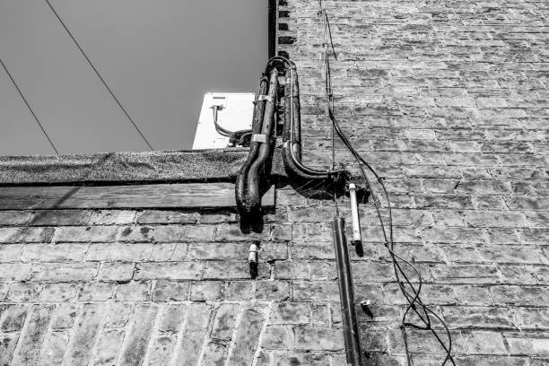 istock Vertical, monochrome view of current and old pipes including an air conditioning unit seen atop of a flat roof behind on old brick-built building. 1237637257