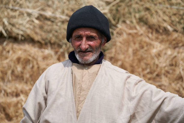 Old farmer man with Hay bales on background. Elderly muslim farmer with haystacks on field, close-up portrait