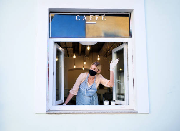 istock Woman with face mask serving coffee through window, shop open after lockdown. 1237667333