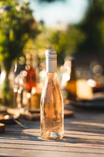 Bottle of cold rose wine on dinner table An unopened bottle of cold rosé wine on a midsummer dinner table in Sweden. Focus on the dripping fresh bottle in the foreground. wet bottle stock pictures, royalty-free photos & images