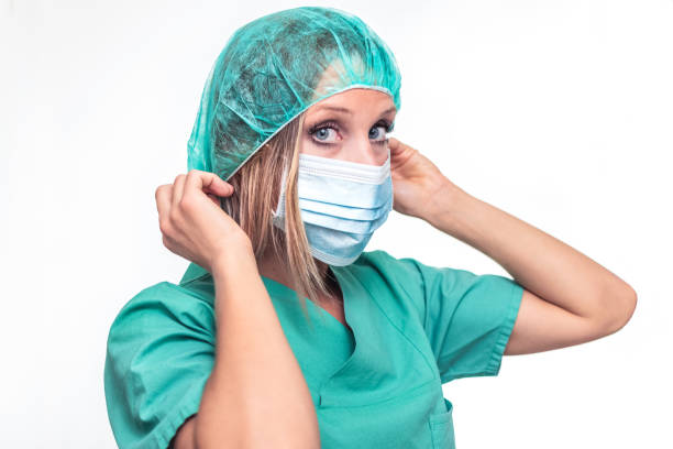 istock A nurse with blue eyes, with green uniform, isolated in a white background, with a head cover on her head, makes the gesture with her hands to wear a mask. 1237692357