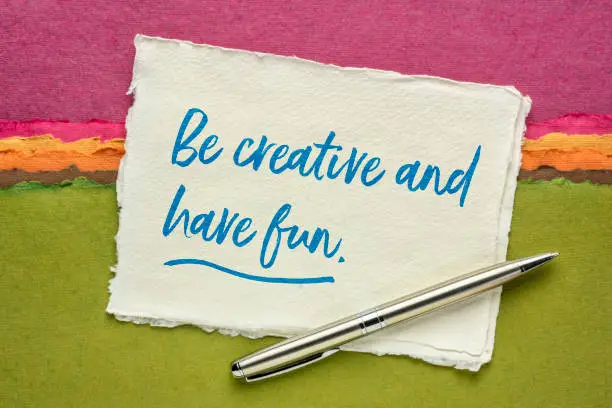 Be creative and have fun inspirational reminder - handwriting on a small sheet of Khadi rag paper against colorful abstract landscape, creativity and personal development concept
