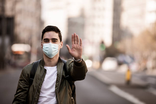 istock Serious young man makes stopping movements, pulls his palm towards the camera, wears a medical mask of the flu, begs him to stay at home so that coronavirus disease does not spread, prevents the virus, 1237723888
