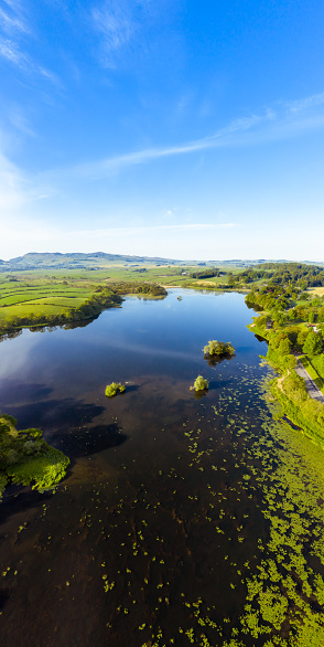 Three images captured by a drone merged to give a vertical panorama of a Scottish loch on a bright spring morning .\nThe loch is in Dumfries and Galloway, south west Scotland.