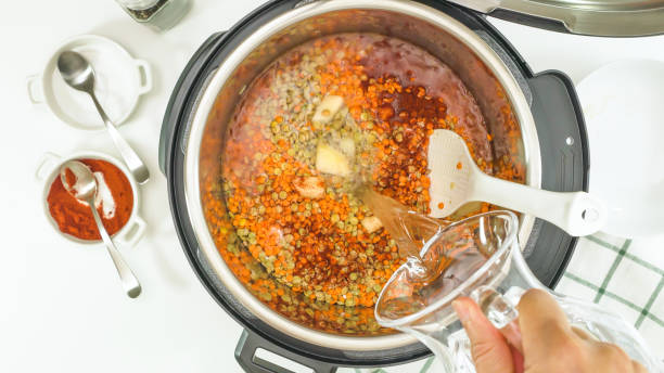 recette de soupe de lentilles multicuise. femme versant l’eau dans le pot, près de la vue d’en haut - carrot close up silverware cutting board photos et images de collection
