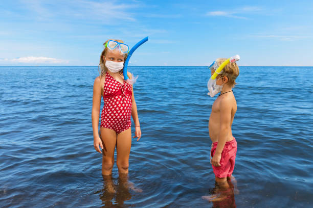 Funny kids in surgical face mask on sea beach Kids in snorkeling mask wear surgical face mask on sea beach. Cancelled cruises, tours due coronavirus COVID 19 world epidemic. Travel ban for family vacation, tourism industry crisis at summer 2020 vacation rental mask stock pictures, royalty-free photos & images