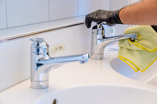 A professional cleaner polishes a bathroom sink and faucet with a yellow micro fiber cloth