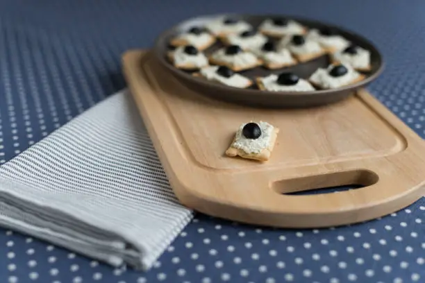 Photo of Plate with crackers with soft cheese and olives on a blue polka dot tablecloth.