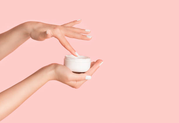 istock Unrecognizable girl applying cream from jar onto her hands against pink background, blank space 1237973485