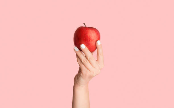 istock Female hand holding ripe red apple on pink background, close up. Panorama 1237975085