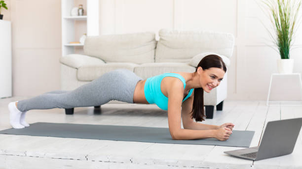 istock Young Woman At Laptop Exercising Doing Plank During Home Workout 1237978317