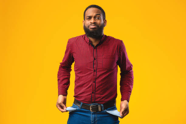 Portrait of black guy showing empty pockets Poverty And Absence Of Money Concept. Unemployed sad black man showing empty pockets, isolated on yellow studio wall empty pockets stock pictures, royalty-free photos & images