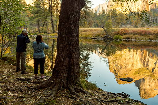 Yosemite, California, USA - October 25, 2018: A couple takes pictures of the reflection of the landscape in the water of the Merced River in Yosemite National Park