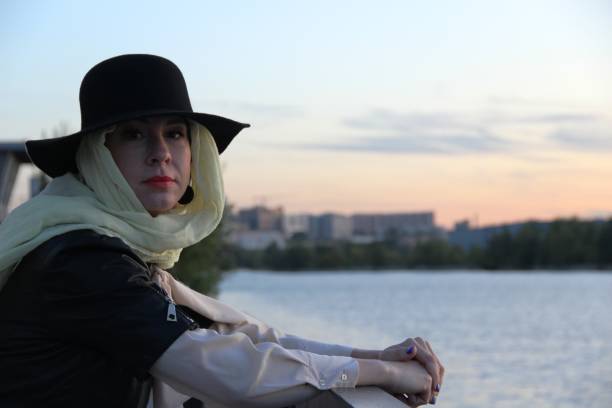 istock woman in a black jacket, a black hat over a beige handkerchief, alone by the river. after self-isolation, portrait without gloves and masks 1237990028