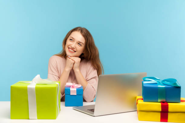 istock Dreamy woman office employee sitting at workplace, smiling friendly surrounded by many gift boxes and thinking 1238007713