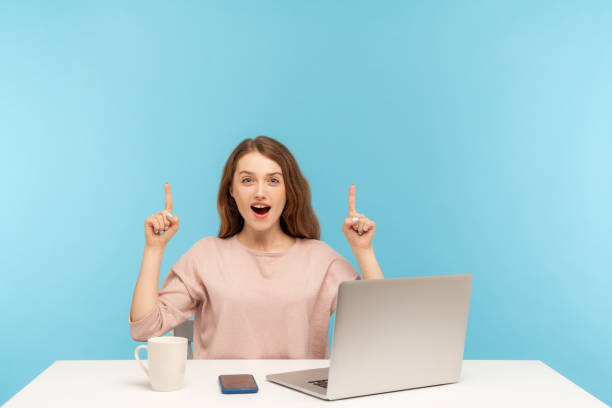 istock Wow, look above at advertisement! Surprised young woman sitting at office workplace with laptop and pointing up 1238007714