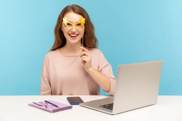 Funny cheerful woman employee covering eyes with paper glasses, wearing humorous masquerade accessory Funny cheerful woman employee covering eyes with paper glasses, wearing humorous masquerade accessory, having fun at workplace while working in office. indoor studio shot isolated on blue background vogue cover stock pictures, royalty-free photos & images