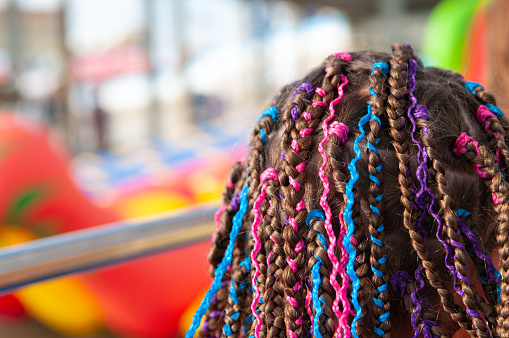 Teen girl's hair with small afro pigtails with bright multicolored ribbons