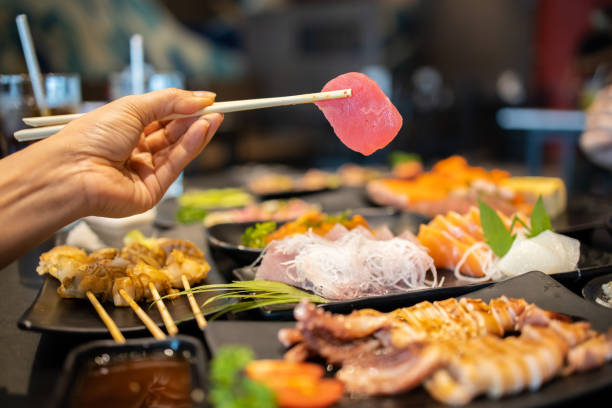 istock Hand holding tuna sashimi using chopsticks, Raw fresh tuna fish sliced served on ice, Japanese food style. 1238045509