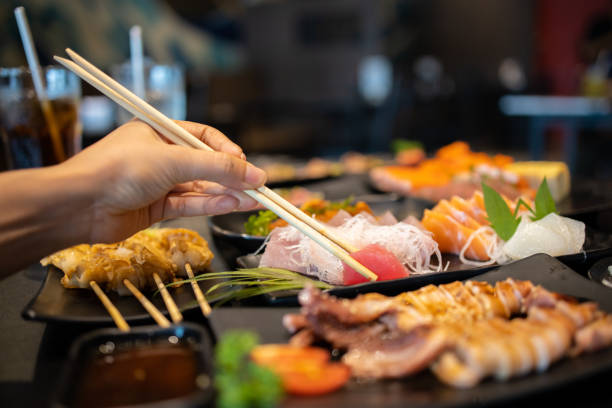 istock Hand holding tuna sashimi using chopsticks, Raw fresh tuna fish sliced served on ice, Japanese food style. 1238045523