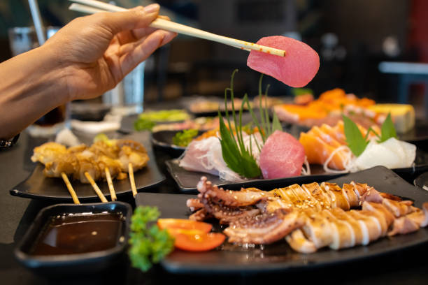 istock Hand holding tuna sashimi using chopsticks, Raw fresh tuna fish sliced served on ice, Japanese food style. 1238046038