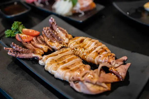 Close up the squid with sweet sauce and sesame seeds on the black plate with blur of the japanese food set. Traditional in Japanese food.