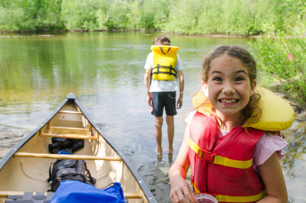 istock Two kids, standing in river water, besides canoe 1238078188