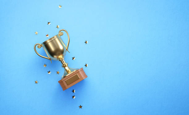 istock Star Shaped Confetti Falling over Gold Cup Sitting over Blue Background 1238087627