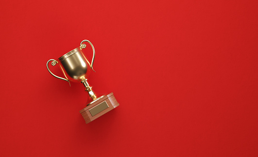 Gold cup sitting over red background. Horizontal composition with copy space. Directly above.