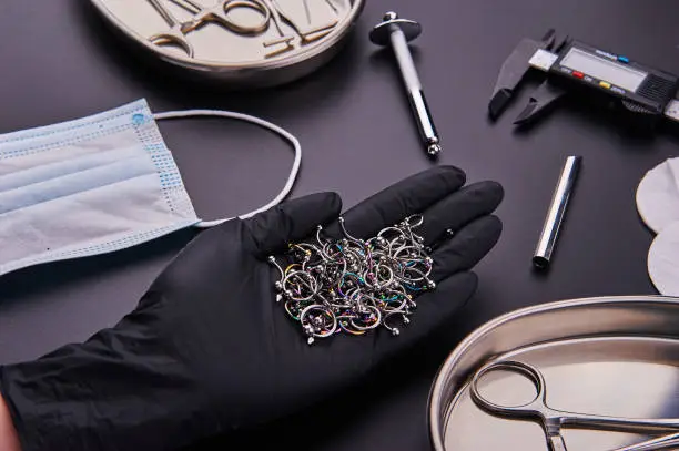 piercer master's hand in a medical black glove holds earrings. Around instrument for piercing and disinfection