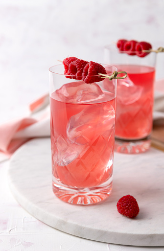 Pink rose cocktails with raspberry in crystal glass on table. Trendy summer iced beverage