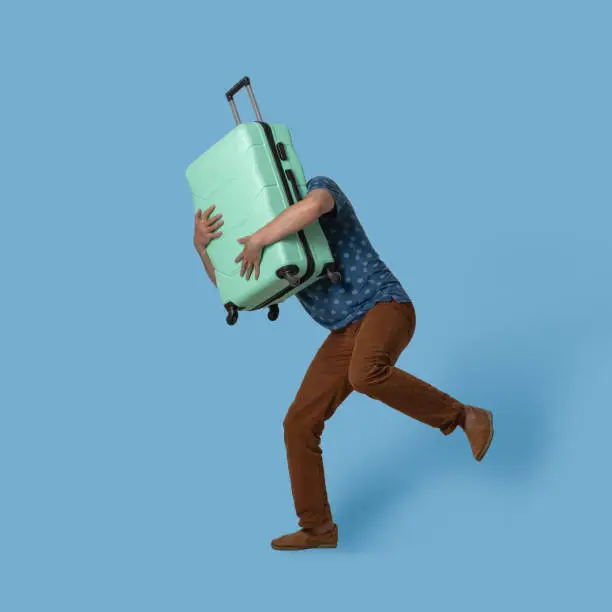 Running man holds plastic suitcase in front of himself. Caucasian traveler with light green suitcase of luggage trying to catch up with plane. Isolated on colored background. Template with textspace.