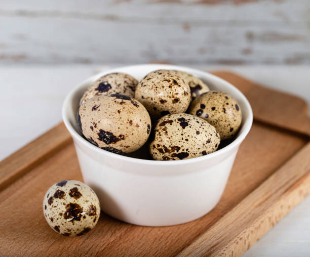 Quail eggs in white bowl on wooden background